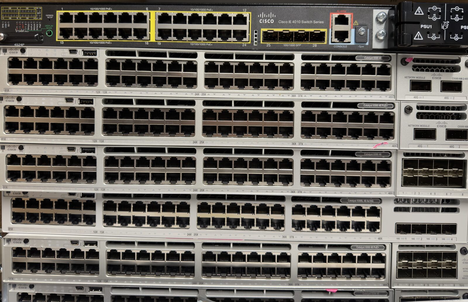 Front view of a stack of Cisco switches, an IE 4010 industrial switch on top and several Catalyst 9300 series switches below, with rows of copper ports and fiber uplink modules