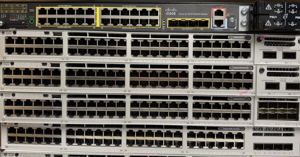 Front view of a stack of Cisco switches with rows of copper ports, an IE 4010 industrial switch on top and Catalyst 9300 series switches below
